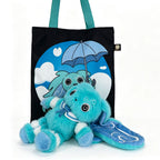 Plush blue Dysautonomia Rabbit toy with floppy ears lies in front of a black tote bag with an umbrella design.