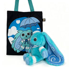 Blue plush Dysautonomia Rabbit sits beside a black tote bag featuring the bunny with an umbrella on a blue background.