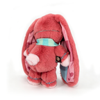 Plush pink awareness rabbit with floppy ears, blue scarf, and heart lining, facing away on a white background.
