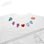 White shirt with colorful gender and planetary sign patches plus a red heart patch arranged near the neckline.