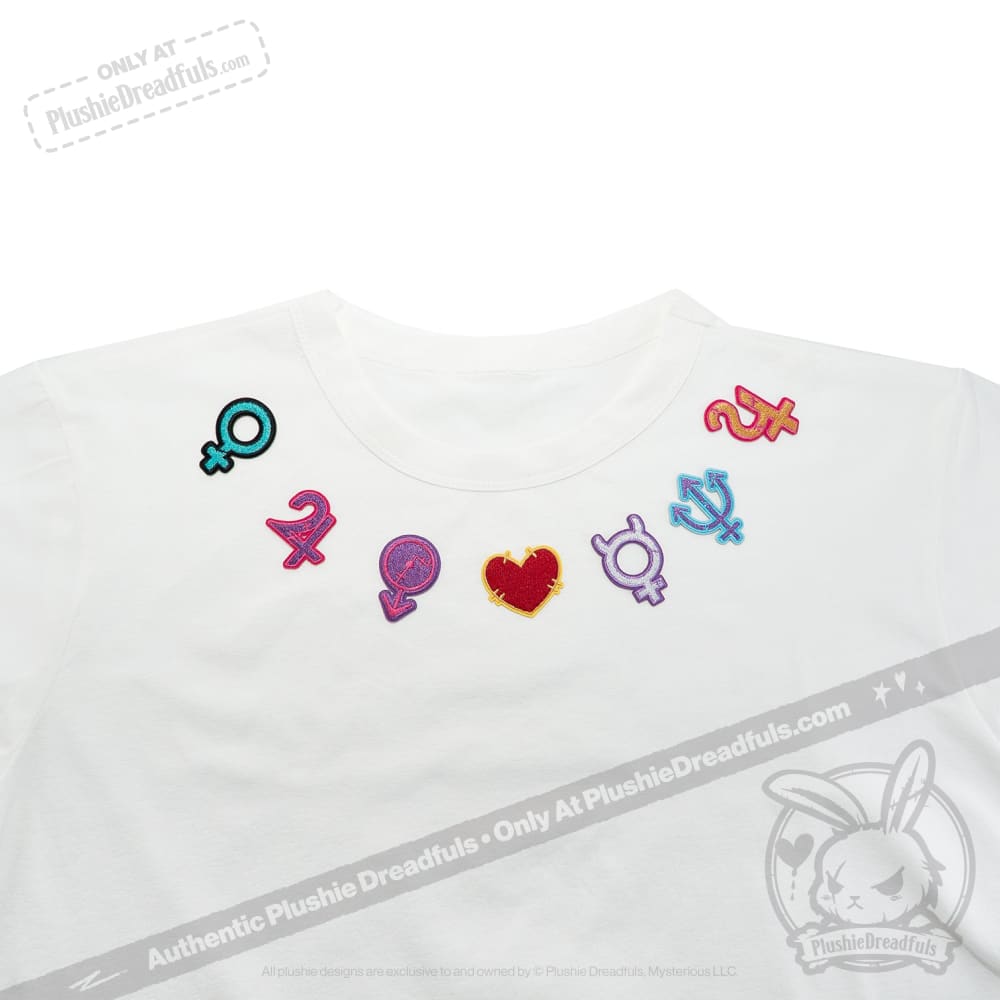 White shirt with colorful gender and planetary sign patches plus a red heart patch arranged near the neckline.