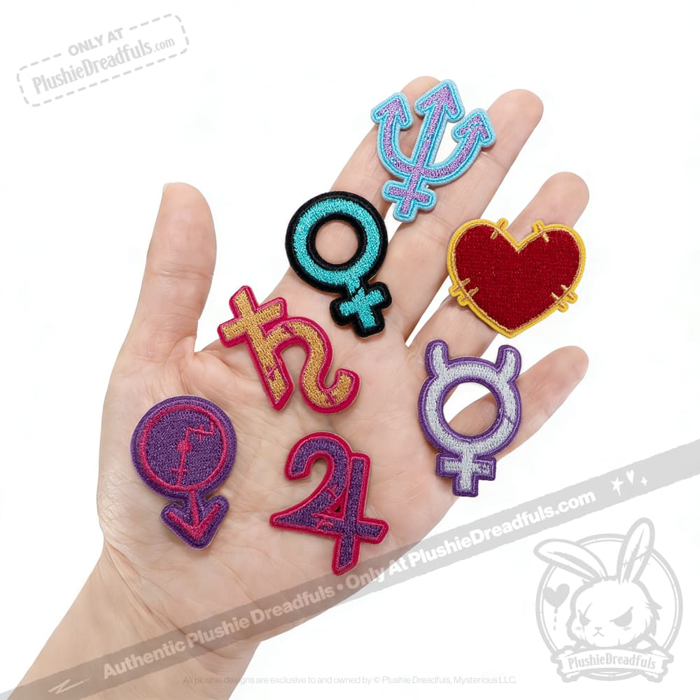 A hand holds seven colorful planetary sign patches, each embroidered with astrology and gender symbols, plus a red heart.