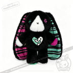 Plush black emotional support bunny with striped ears, colorful patches, and a heart design on its chest, sitting upright.