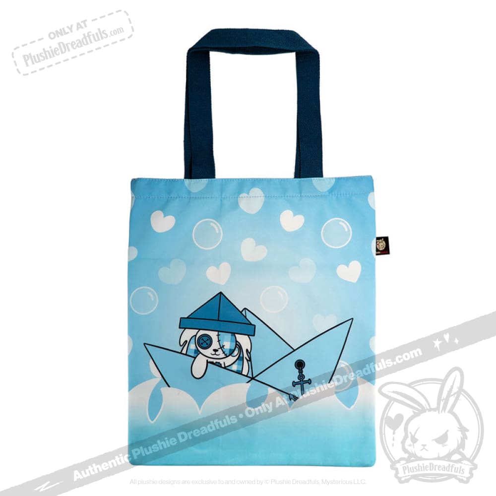Blue tote bag with dark handles, featuring a Seas of Love cartoon dog sailor in a paper boat, hearts, and bubbles background.