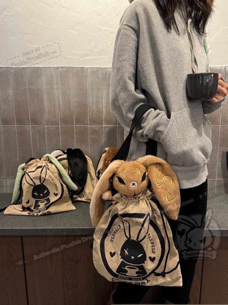 Person in a gray hoodie holds a mug and a canvas bag with Latte Lapin plushies and black bunny print on the front.