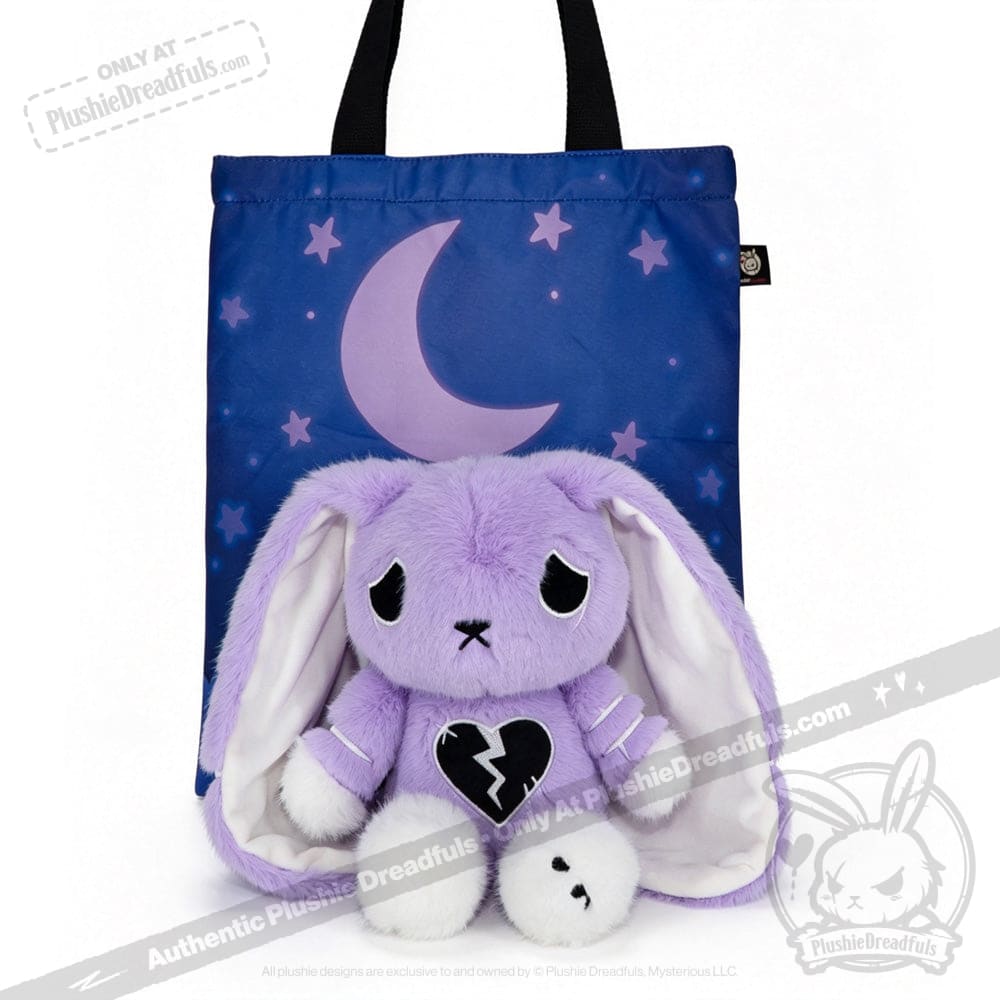 A purple plush bunny with a broken heart and semicolon symbol sits by a blue tote with crescent moon and stars.