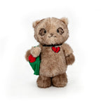 A Plushie Dreadfuls teddy bear with a red broken heart on its chest holds a green bag with a red heart inside.