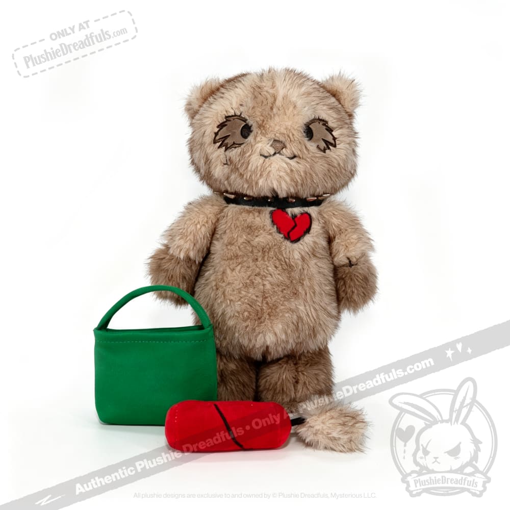 A brown Plushie Dreadfuls cat with broken heart patch, green bag, and red toy sits on white—find it at plushiedreadfuls.com.
