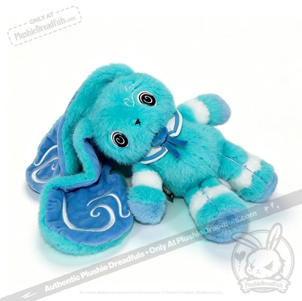 A fluffy blue Dysautonomia Rabbit plush with floppy ears, a blue bow, and a cape is lying on its side.