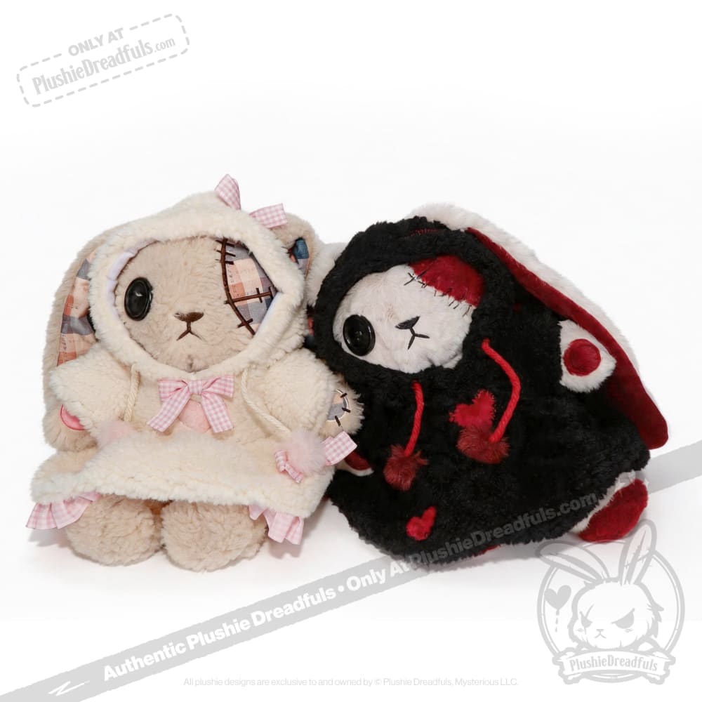 Two Plushie Dreadfuls bunnies in patchwork clothes, one white with pink bows, one black with red hearts, sit together.