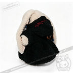 A Plushie Dreadfuls toy in a black and cream plushie hoodie with red embroidery, facing away from the camera.