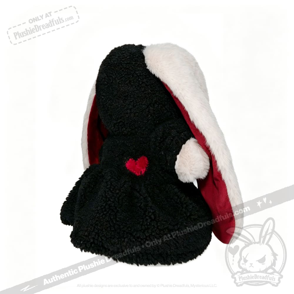 A Plushie Dreadfuls bunny with black fur, a red heart, and long white and red ears sits facing away.