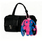 Black handbag with two front pockets and a Gemini Rabbit plushie keychain attached to one handle.