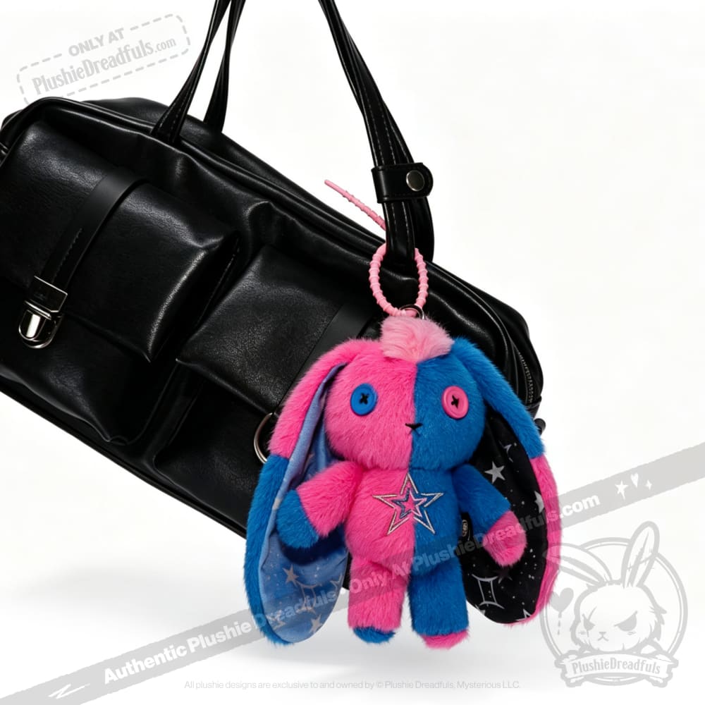 A black handbag with a Gemini Rabbit plushie keychain in pink and blue hanging from one of its handles.