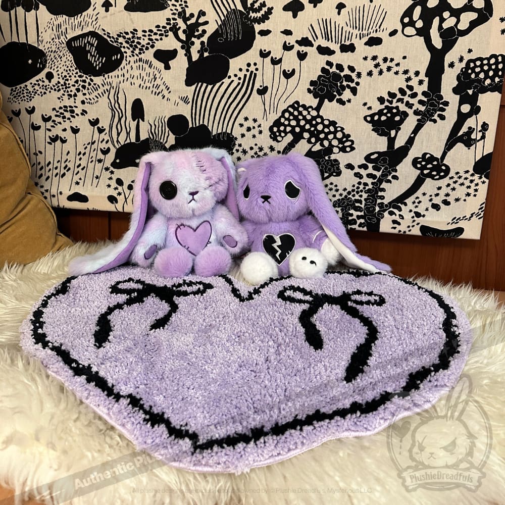 Two purple plush bunnies sit on a purple goth floor rug, bows on top, with a black and white forest tapestry behind.