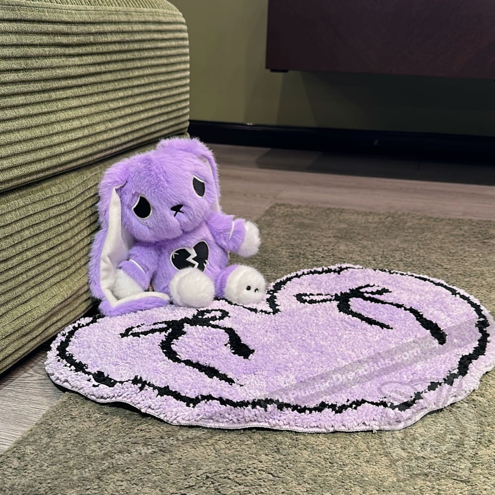 A purple plush bunny with a heart sits by a green couch next to a purple goth floor rug shaped like a heart.