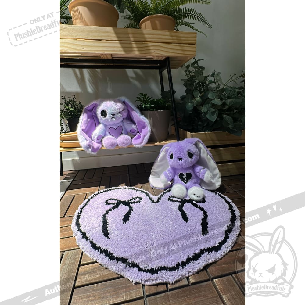 Two purple bunny plush toys with hearts sit on a purple goth floor rug, surrounded by potted plants.