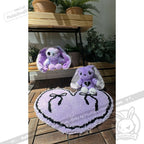 Two purple bunny plush toys with hearts sit on a purple goth floor rug, surrounded by potted plants.