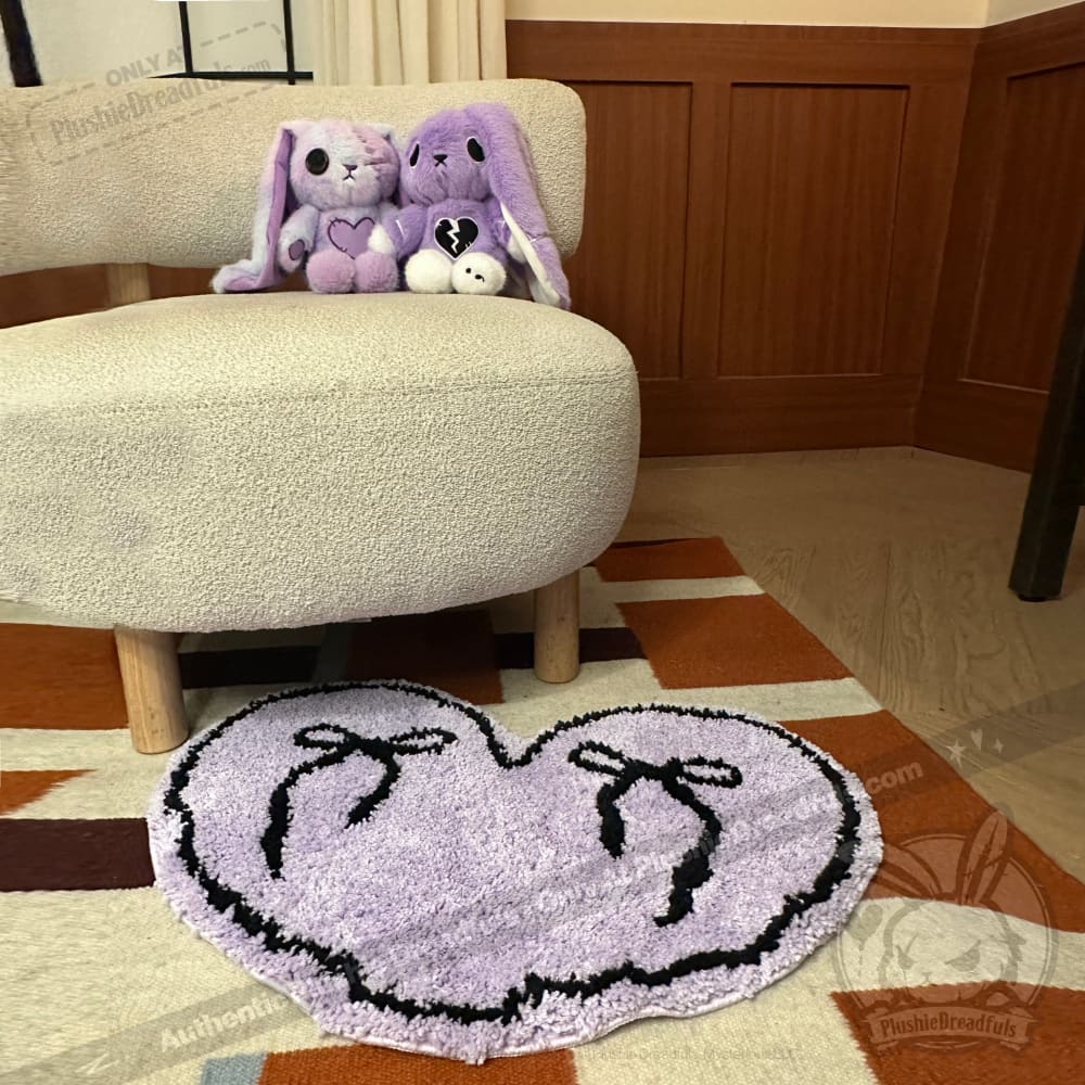 Two purple stuffed bunnies sit on a chair with a purple goth floor rug shaped like a heart in front of them.