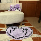 Two purple stuffed bunnies sit on a chair with a purple goth floor rug shaped like a heart in front of them.