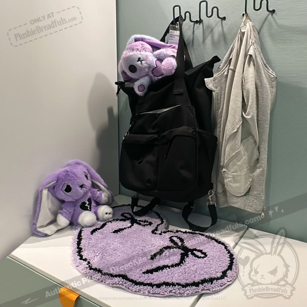 Black backpack, grey vest, and purple bunny plushies with a purple goth floor rug on a white surface.