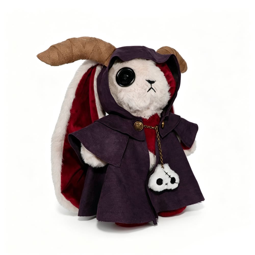 A Plushie Dreadfuls rabbit in a horned cloak holds a skull charm, exuding mysterious plushie magic.