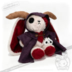 Plushie Dreadfuls horned cloak bunny, one button eye, purple cloak, holding a stitched doll on white background.