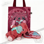 A pink tote bag with a cartoon face, plus an awareness rabbit plushie and matching bunny-eared blanket in front.