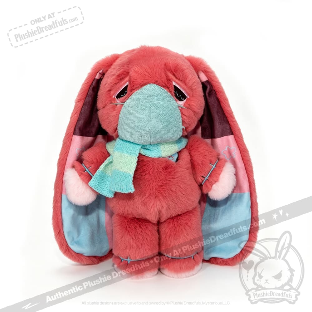 A pink awareness rabbit plushie with long ears, turquoise scarf, and face mask sits against a white background.
