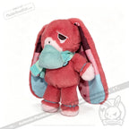 Pink plush bunny with long ears, a teal scarf and mask—an awareness rabbit plushie symbolizing chronic illness.