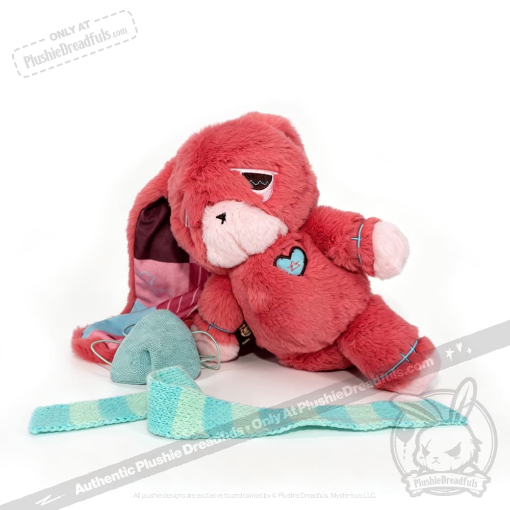 Pink plush bear with a heart patch, a symbolic chronic illness gift, sits by a blue and white knitted scarf and yarn.