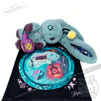Blue Pisces Rabbit plush with lantern lounges on black cloth adorned with a vibrant cosmic sea turtle illustration.