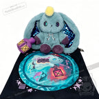 Blue Pisces Rabbit plush with shiny blue ears sits on a black bag featuring its matching fantasy illustration.