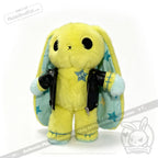 Plush yellow bunny with large black eyes, blue stars, and a faux leather jacket against a white backdrop.