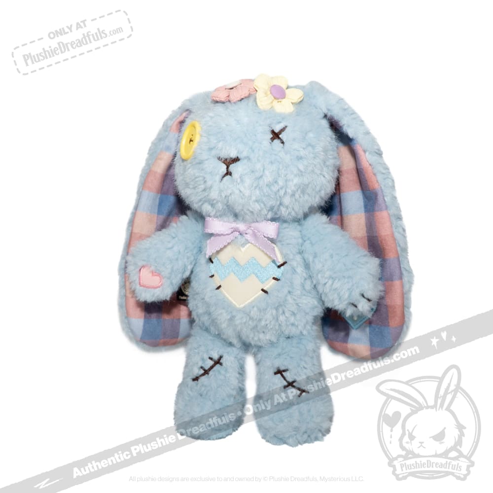 Blue Plushie Dreadful bunny with plaid ears, yellow button eye, and flowers, standing upright on a white background.
