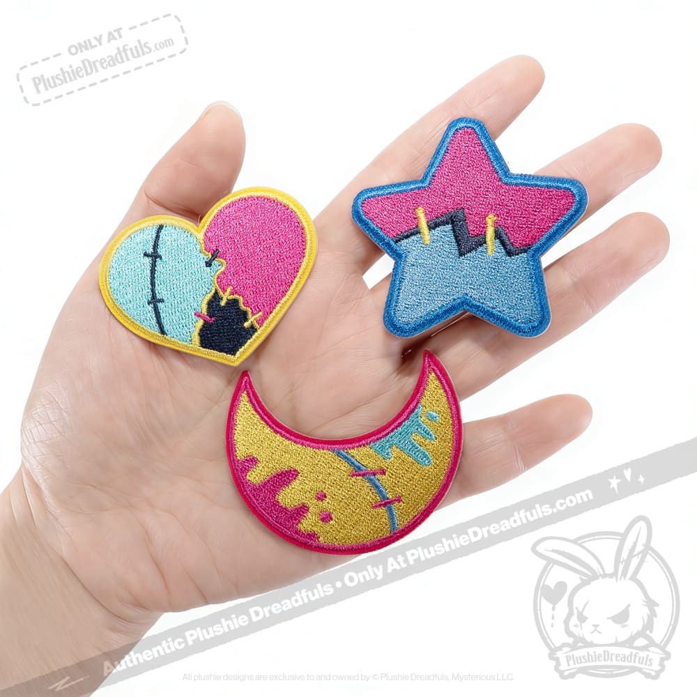 A hand holds three night sky patches—heart, star, and crescent moon—each with colorful abstract designs.