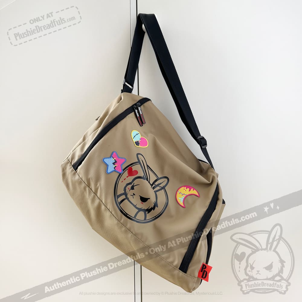 Tan messenger bag with a cartoon bunny face and cute iron on patches, hanging on a white door.