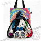 Plushie black-and-white bunny with a top hat sits before a rainbow tote, embracing ADHD Mad Hatter vibes and acceptance.