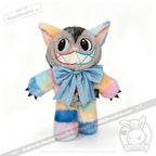 Victorian McGee's Autism Acceptance Cheshire Cat - Plush Stuffed Animal features rainbow pastel fur, big pointed ears, large eyes, black claws, a wide grin with rainbow teeth, and a big blue bow around its neck. Standing against a white background, this whimsical plush nods to Alice in Wonderland while celebrating autism acceptance.
