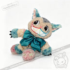 A whimsical Victorian McGee's Autism Acceptance Cheshire Cat plush stuffed animal sits against a white background, featuring pastel blue, pink, and cream fur, large embroidered eyes, a wide colorful stitched smile, black claws, and a big teal bow around its neck—a delightful nod to Alice in Wonderland collectibles that celebrates autism acceptance.
