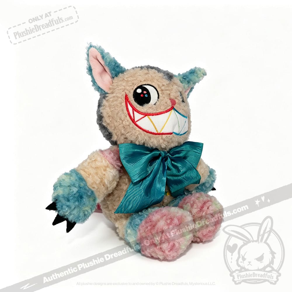 A vibrant Victorian McGee's Autism Acceptance Cheshire Cat plush stuffed animal—with multicolored fur, oversized pointy ears, a broad toothy grin, expressive large eyes, and a teal bow around its neck—rests on a white background, joyfully celebrating autism acceptance.
