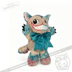 Victorian McGee's Autism Acceptance Cheshire Cat - Plush Stuffed Animal features a cheerful upright cat with cartoonish eyes, pointy ears, and soft blue, pink, and beige fur. Adorned with a large turquoise bow around its neck, this whimsical plush toy is inspired by Alice in Wonderland and brings inclusive charm to any collection.
