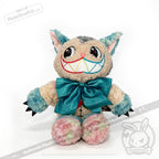 A whimsical, multicolored plush inspired by Alice in Wonderland, the Victorian McGee's Autism Acceptance Cheshire Cat - Plush Stuffed Animal features big eyes, a wide rainbow-stitched grin, pastel-hued pointy ears and paws with black claws. Accented with a large teal bow, it sits charmingly against a white background—a playful tribute to autism acceptance.