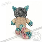 A plush stuffed animal named Victorian McGee's Autism Acceptance Cheshire Cat is displayed from the back against a white background, featuring a gray head, cream-colored body, blue and pink accents, pointy ears, and a long, multicolored tail.