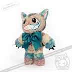 Victorian McGee's Autism Acceptance Cheshire Cat - Plush Stuffed Animal features a wide, toothy grin, colorful pastel fur, large blue bow, pointy ears, and black claws. Inspired by the Alice in Wonderland plush collection, this plush cat showcases embroidered facial features and stands upright on a white background—serving as a whimsical symbol of autism acceptance.