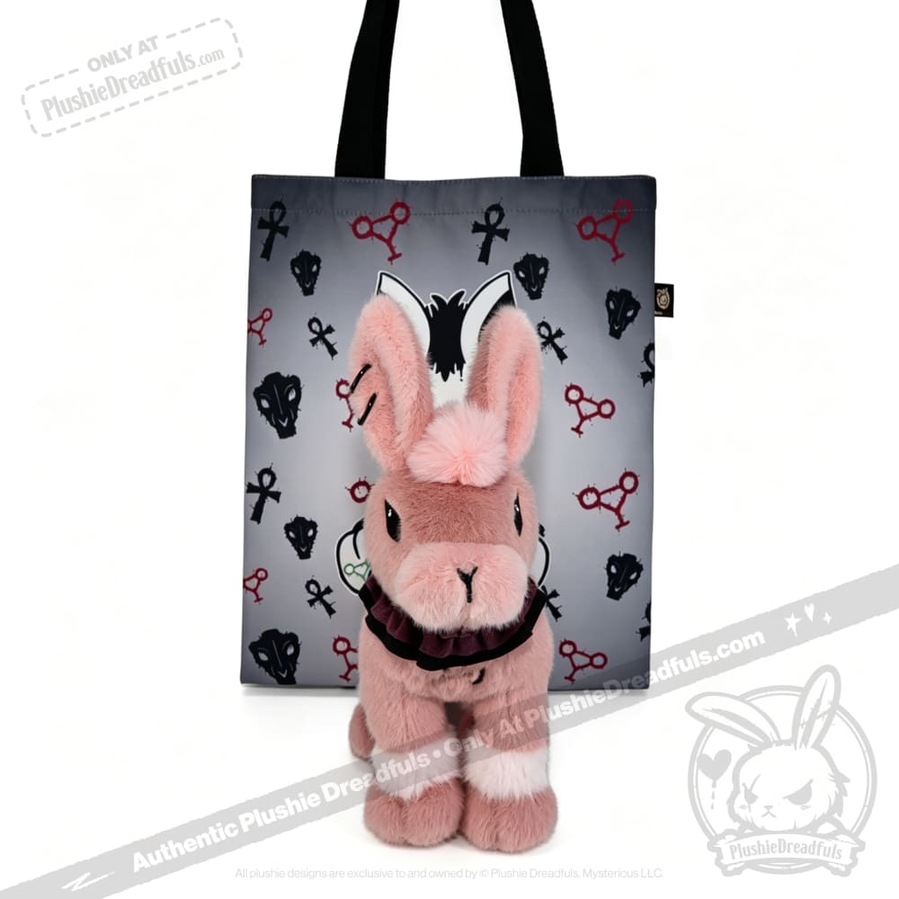 A pink plush bunny sits in front of a gray tote from plushiedreadfuls.com, a limited edition plushie release.